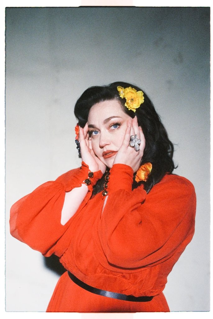 A woman in a vibrant red dress with yellow flowers in her hair touches her face with both hands in Williamson County, Tennessee.