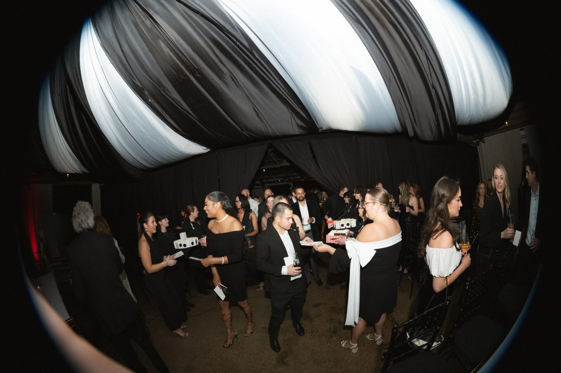 A lively party with people mingling under a black and white striped tent in Williamson County, Tennessee.