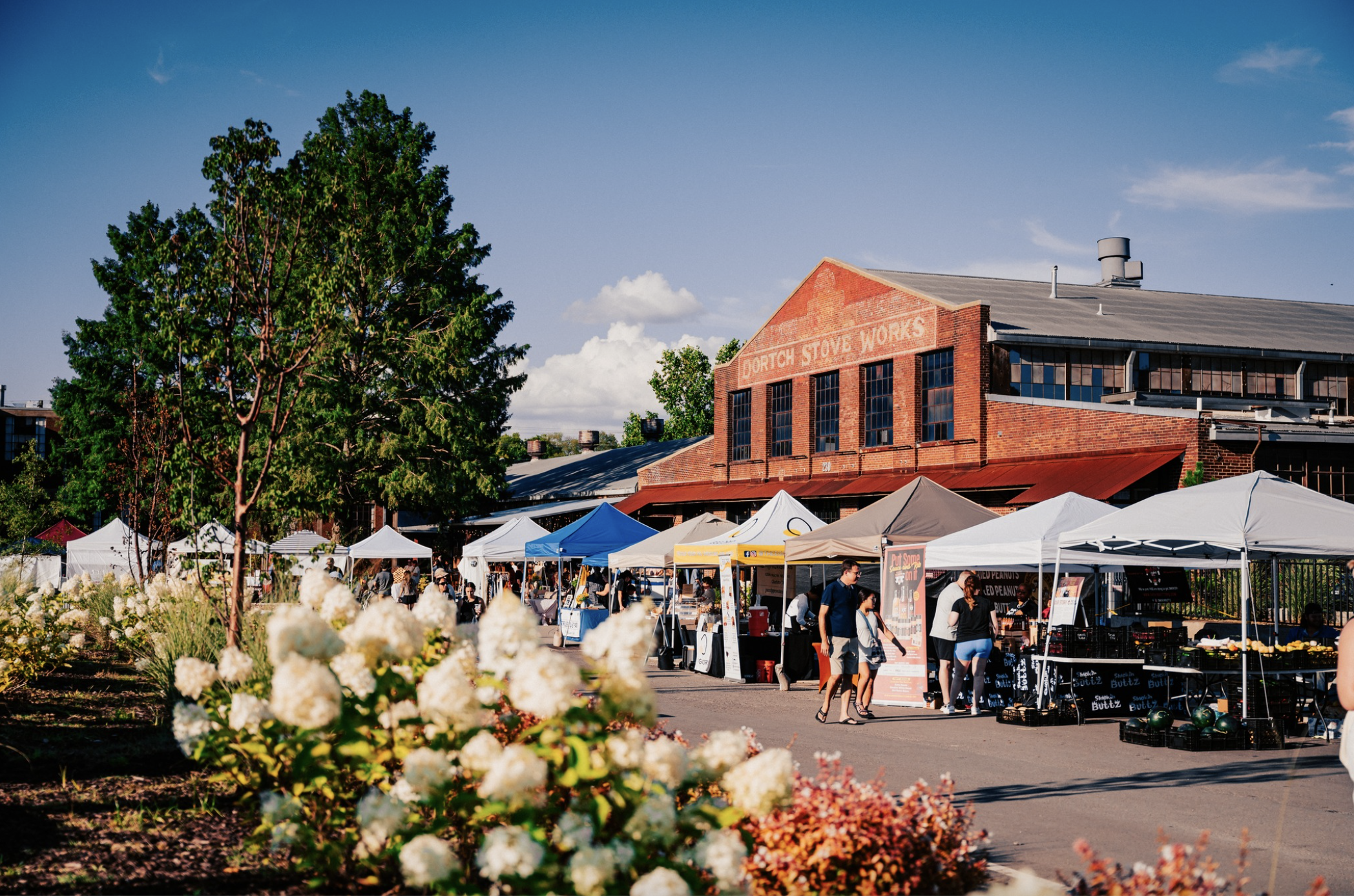 Outdoor market with colorful tents, flowers, and people shopping under a clear blue sky in Williamson County, Tennessee.