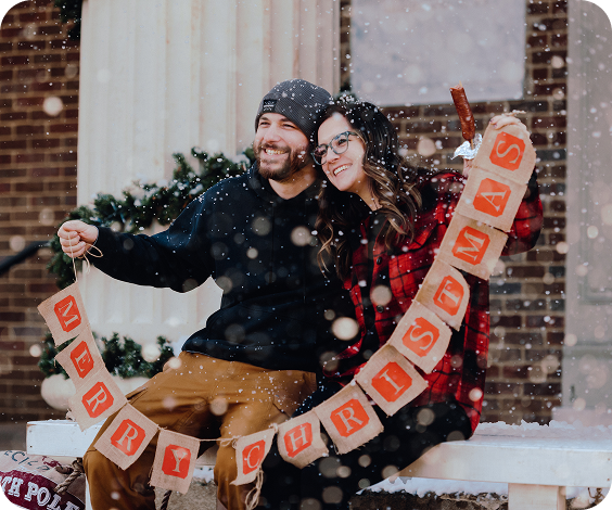 A couple sits on a snowy bench, holding a 'Merry Christmas' banner in Williamson County, Tennessee.