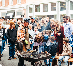Crowd gathers around blacksmith demonstrating traditional metalworking techniques with fire and hammer in Williamson County, Tennessee.