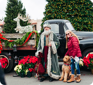 Santa Claus, accompanied by a woman and two dogs, stands beside a decorated truck and Christmas tree in Williamson County, Tennessee.