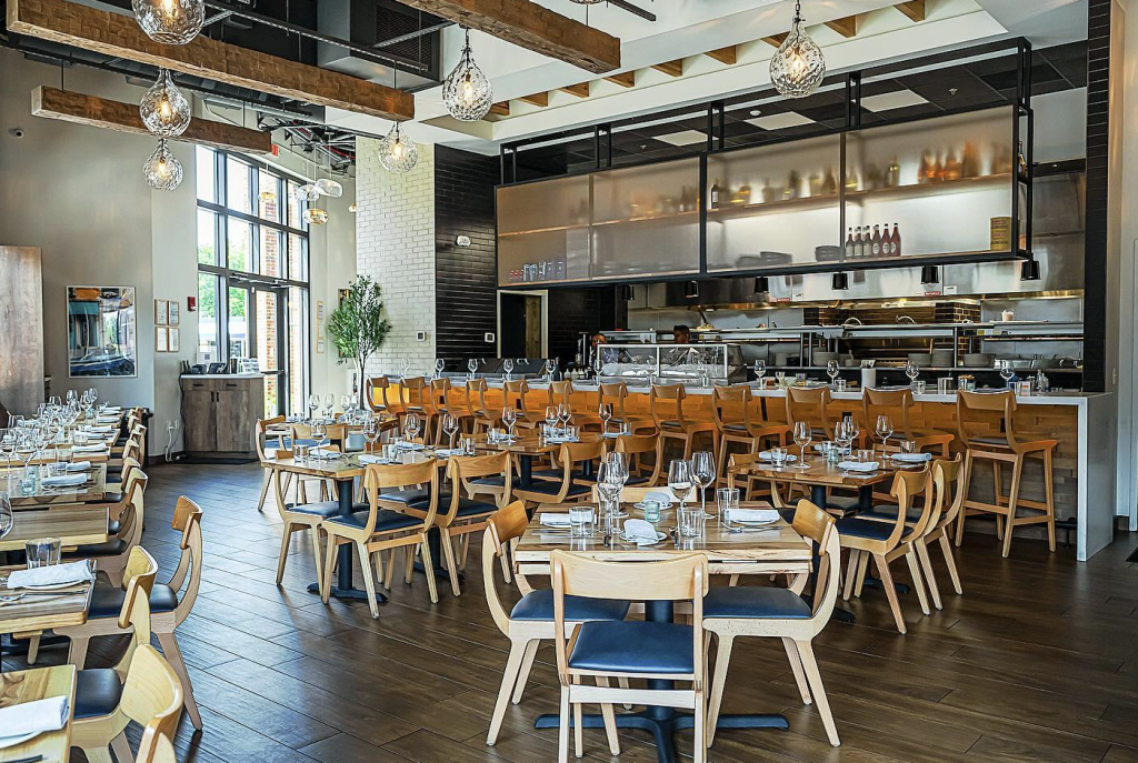 Modern restaurant interior with wooden tables, chairs, and a glass-walled kitchen in Williamson County, Tennessee.