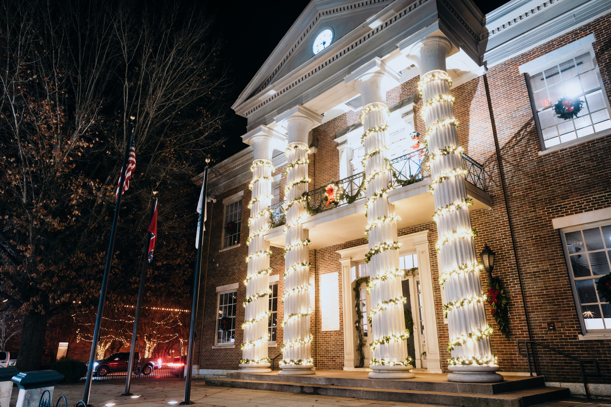 A beautifully lit historic building adorned with white columns wrapped in twinkling Christmas lights, creating a festive atmosphere against the night sky in Williamson County, Tennessee.