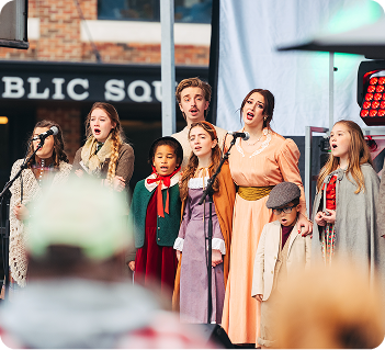 A diverse group of children and adults dressed in period costumes perform a musical number on an outdoor stage in Williamson County, Tennessee.