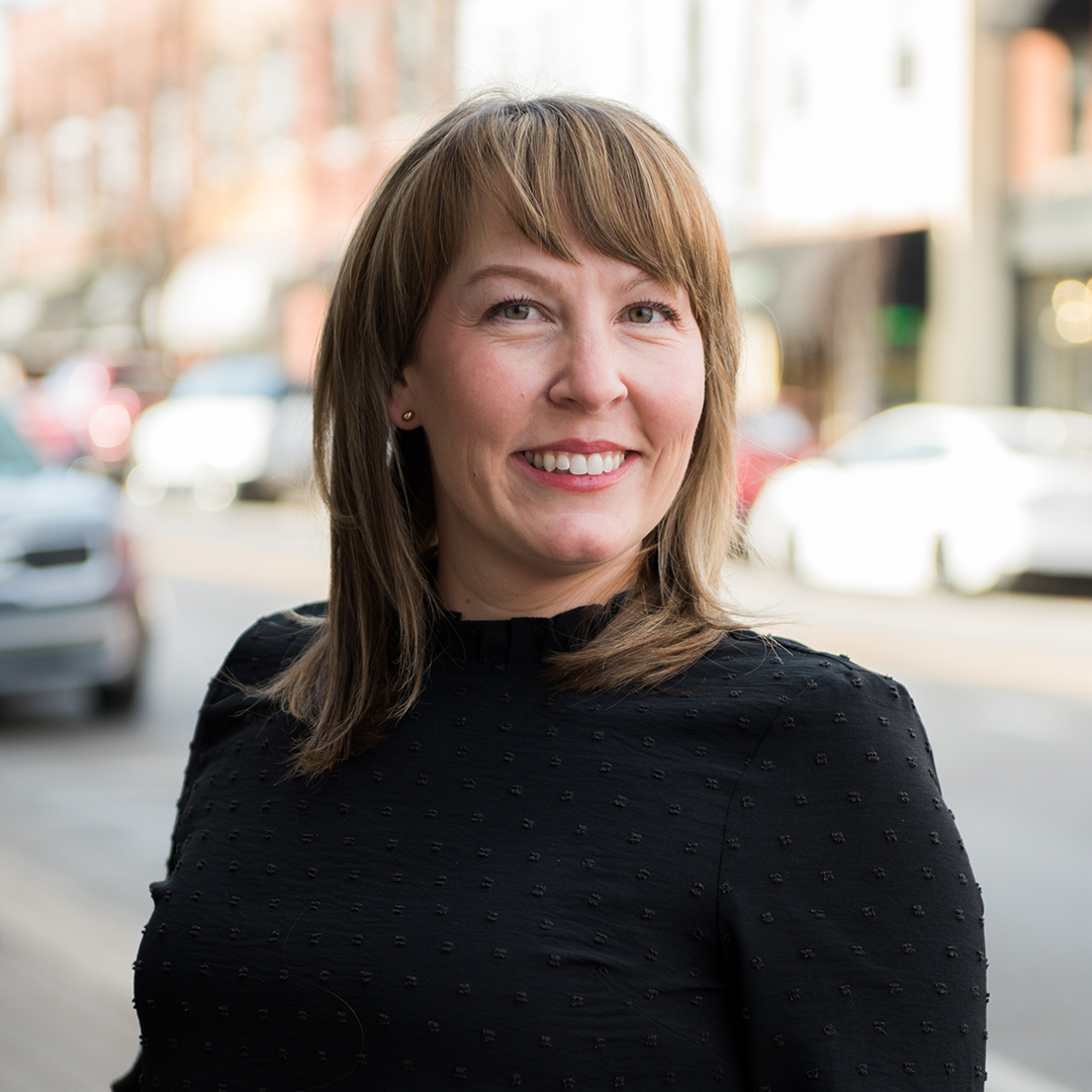 A woman with shoulder-length brown hair and bangs is smiling warmly at the camera, wearing a black top with small white dots in Williamson County, Tennessee.