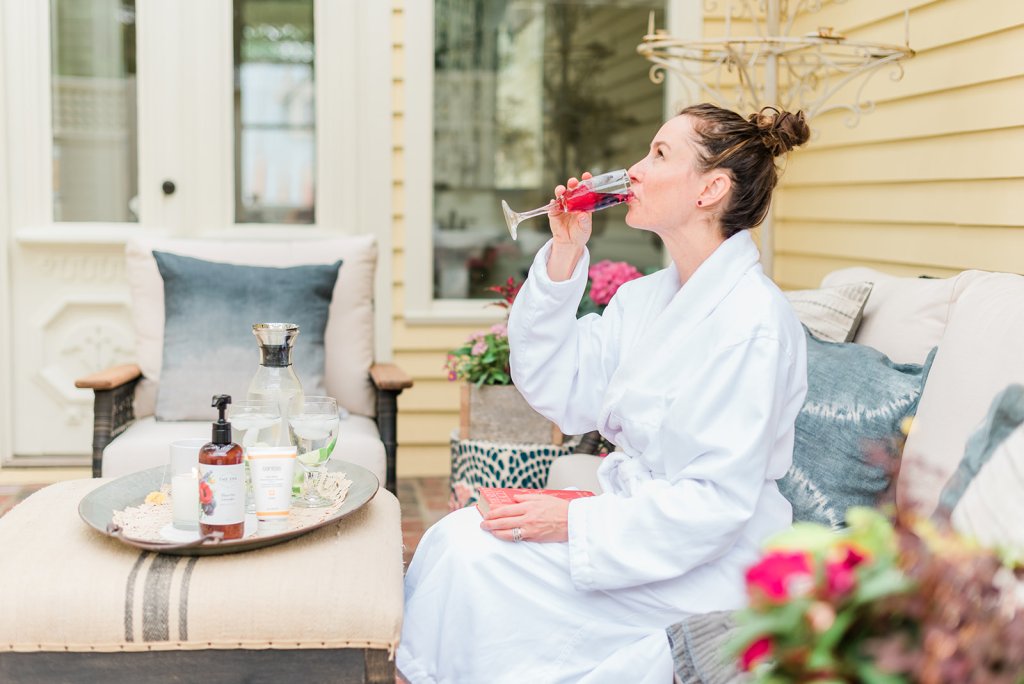 A woman in a white robe enjoys a glass of red wine on a cozy outdoor patio, surrounded by elegant furniture and lush greenery in Williamson County, Tennessee.