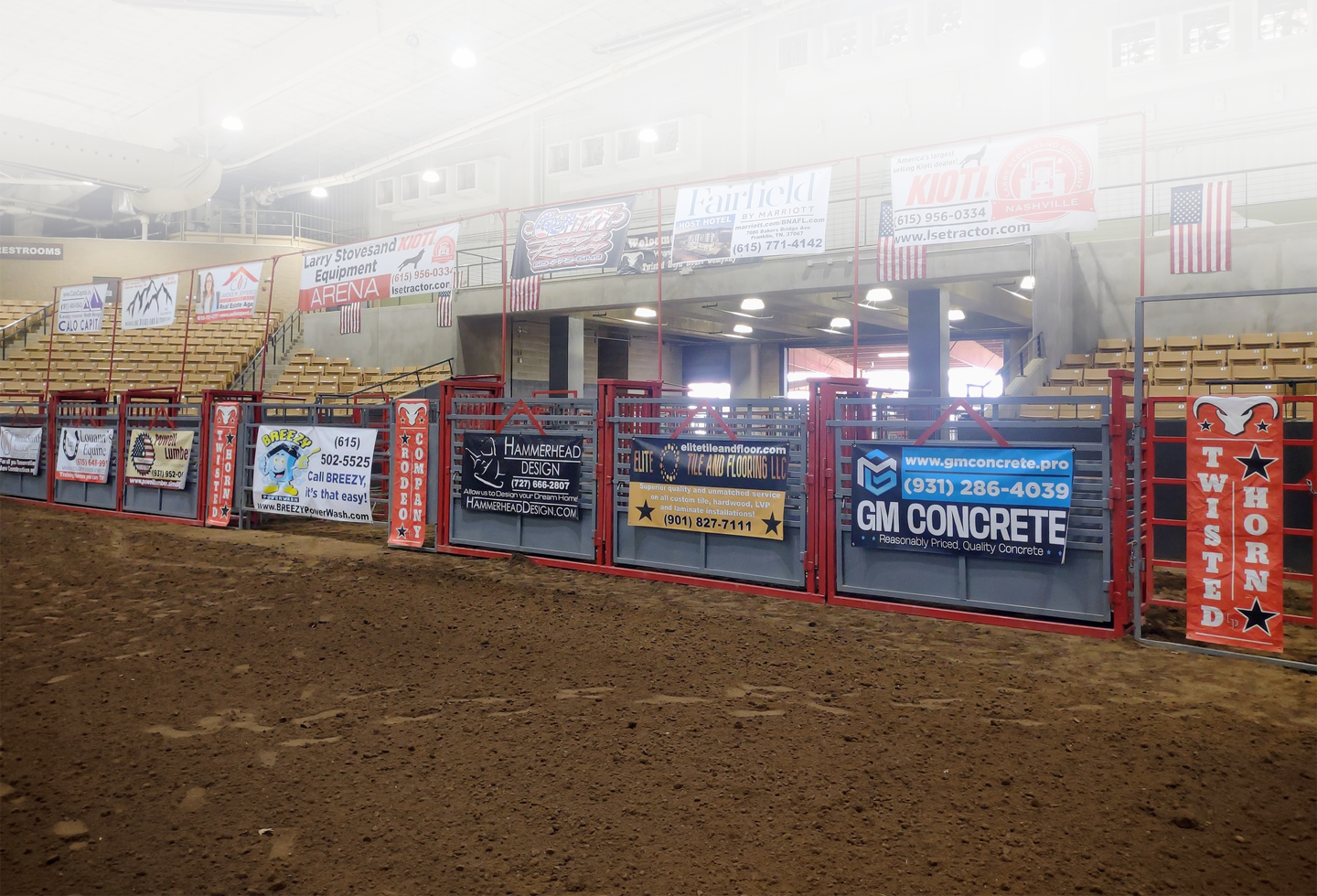 An indoor rodeo arena with red and blue metal fencing, dirt floor, and numerous advertising banners hanging from the walls and ceiling in Williamson County, Tennessee.