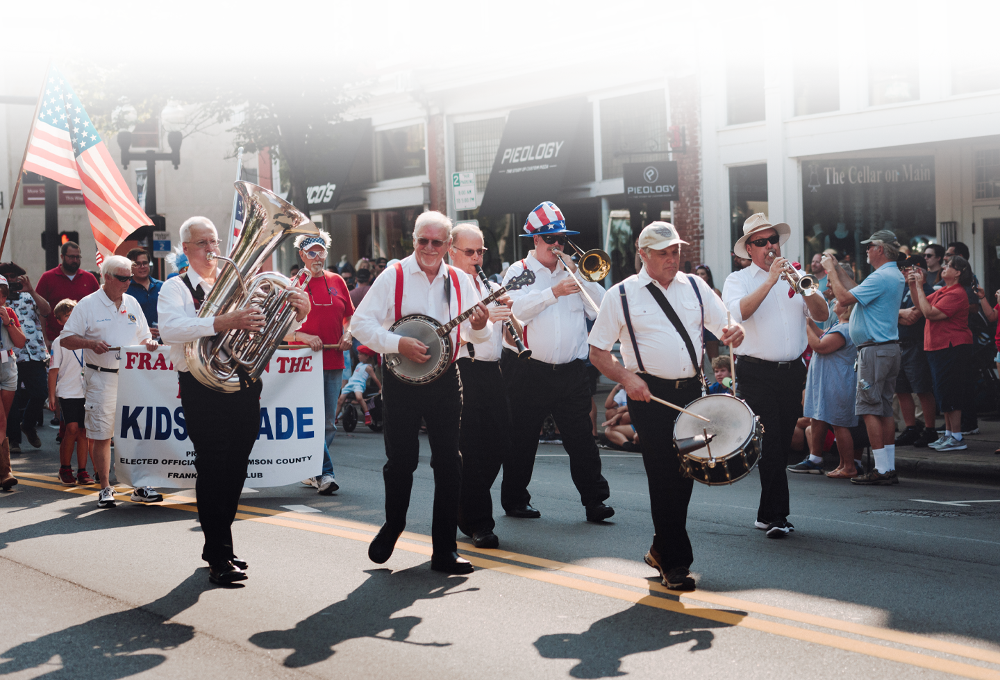A lively parade featuring a marching band dressed in patriotic attire, playing brass and percussion instruments, with an American flag prominently displayed in Williamson County, Tennessee.