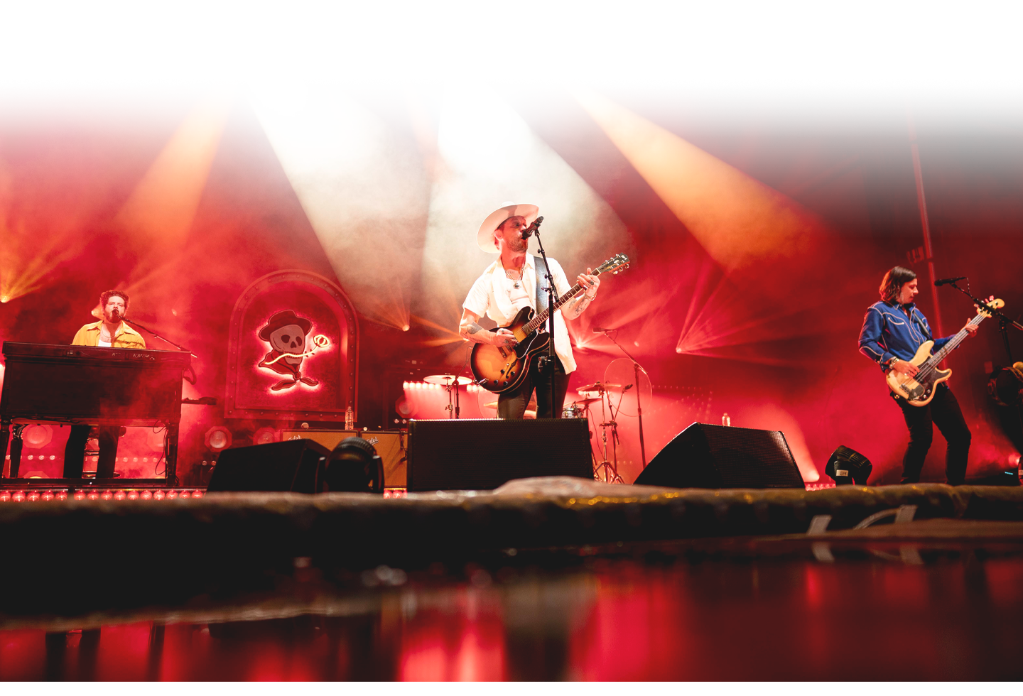 A dynamic rock band performs on stage, illuminated by vibrant red and orange stage lights, with musicians playing guitar, piano, and drums in Williamson County, Tennessee.