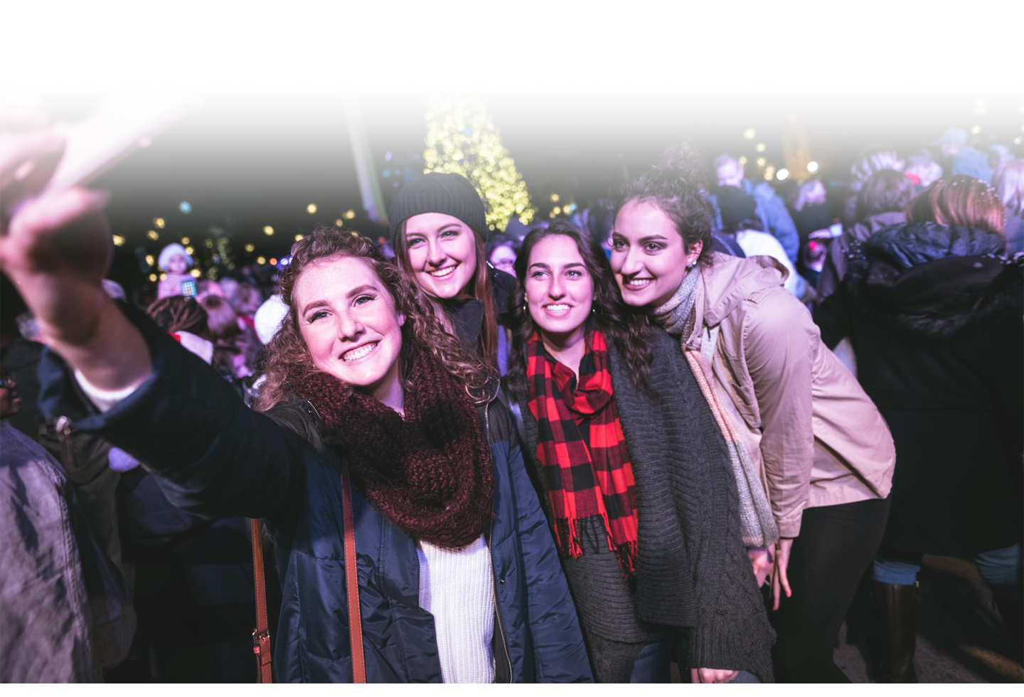 Four women in winter attire take a selfie in front of a brightly lit Christmas tree at a festive outdoor event in Williamson County, Tennessee.