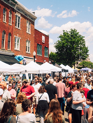 A bustling outdoor market fills a city street with people browsing white tents and enjoying a sunny day in Williamson County, Tennessee.
