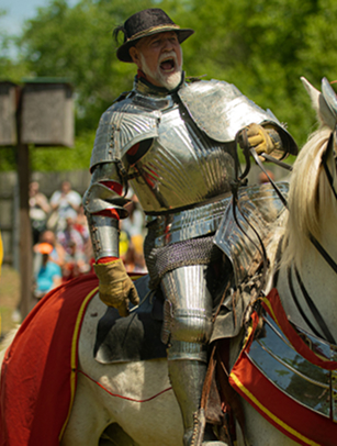 A knight in full armor rides a white horse adorned with red and gold trappings, shouting with excitement as spectators watch from the sidelines in Williamson County, Tennessee.