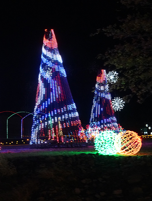 Two towering Christmas trees adorned with vibrant, colorful lights stand tall against the night sky, accompanied by illuminated spheres and arches in the foreground in Williamson County, Tennessee.