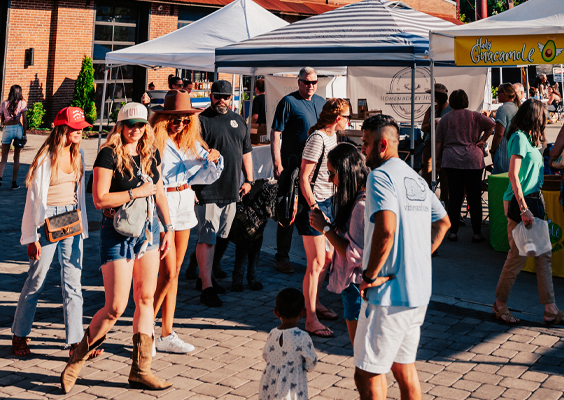 A lively outdoor market scene with people shopping, eating, and socializing under colorful tents in Williamson County, Tennessee.