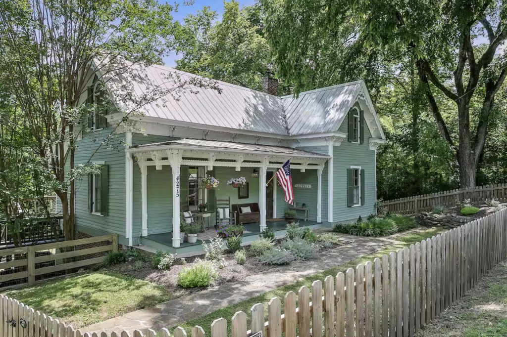A charming two-story Victorian-style house with a wrap-around porch, surrounded by lush greenery and a white picket fence in Williamson County, Tennessee.
