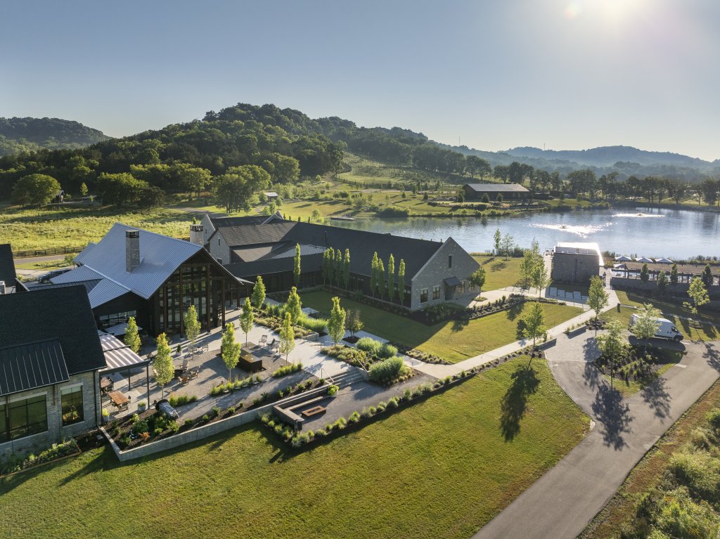 An aerial view of a modern, multi-building complex nestled among lush green hills and a serene lake, with a network of pathways and landscaped gardens in Williamson County, Tennessee.