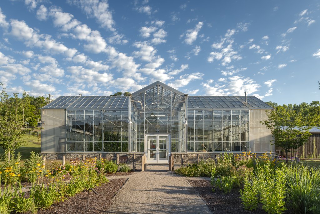 A modern greenhouse with a glass facade and a triangular roof, surrounded by lush gardens and a clear blue sky with scattered clouds in Williamson County, Tennessee.