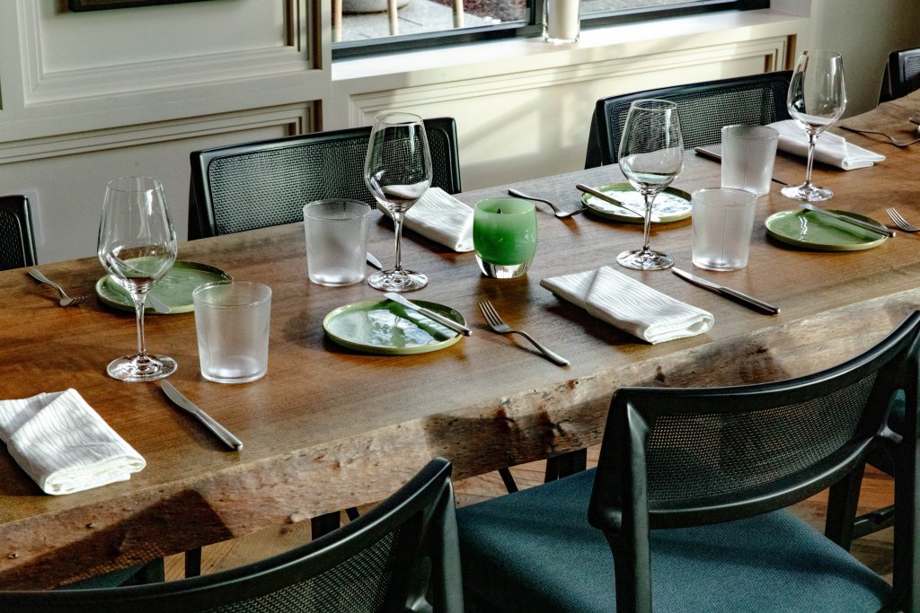 A rustic wooden dining table is set with elegant green and clear glassware, white napkins, and silverware, ready for a meal in Williamson County, Tennessee.