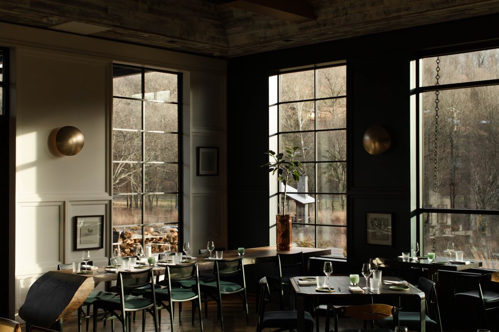 A dimly lit restaurant interior with large windows showcasing a serene outdoor view of trees and a rustic building in Williamson County, Tennessee.