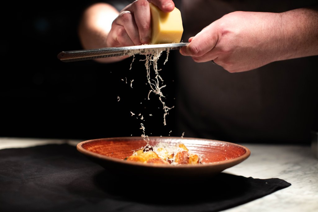 A chef's hands skillfully grate a block of cheese over a rustic dish, creating a shower of golden shavings that cascade onto the plate in Williamson County, Tennessee.