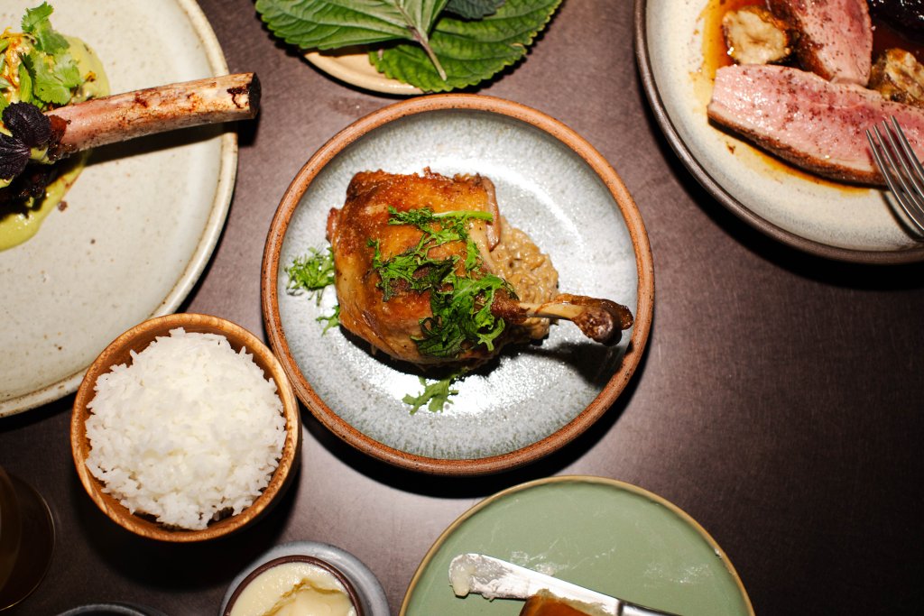 A variety of dishes including a crispy chicken leg, a bowl of white rice, and a plate of thinly sliced meat with a rich sauce, all presented on a dark wooden table in Williamson County, Tennessee.