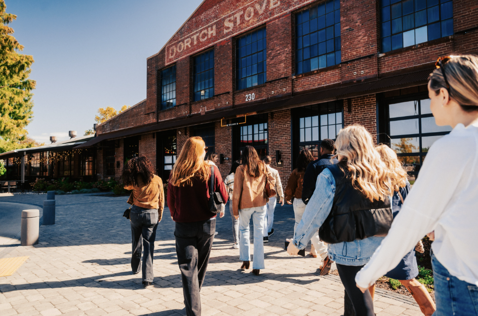 A group of people walks past a historic brick building with large windows and the faded sign 'Dorch Stove' on its facade in Williamson County, Tennessee.