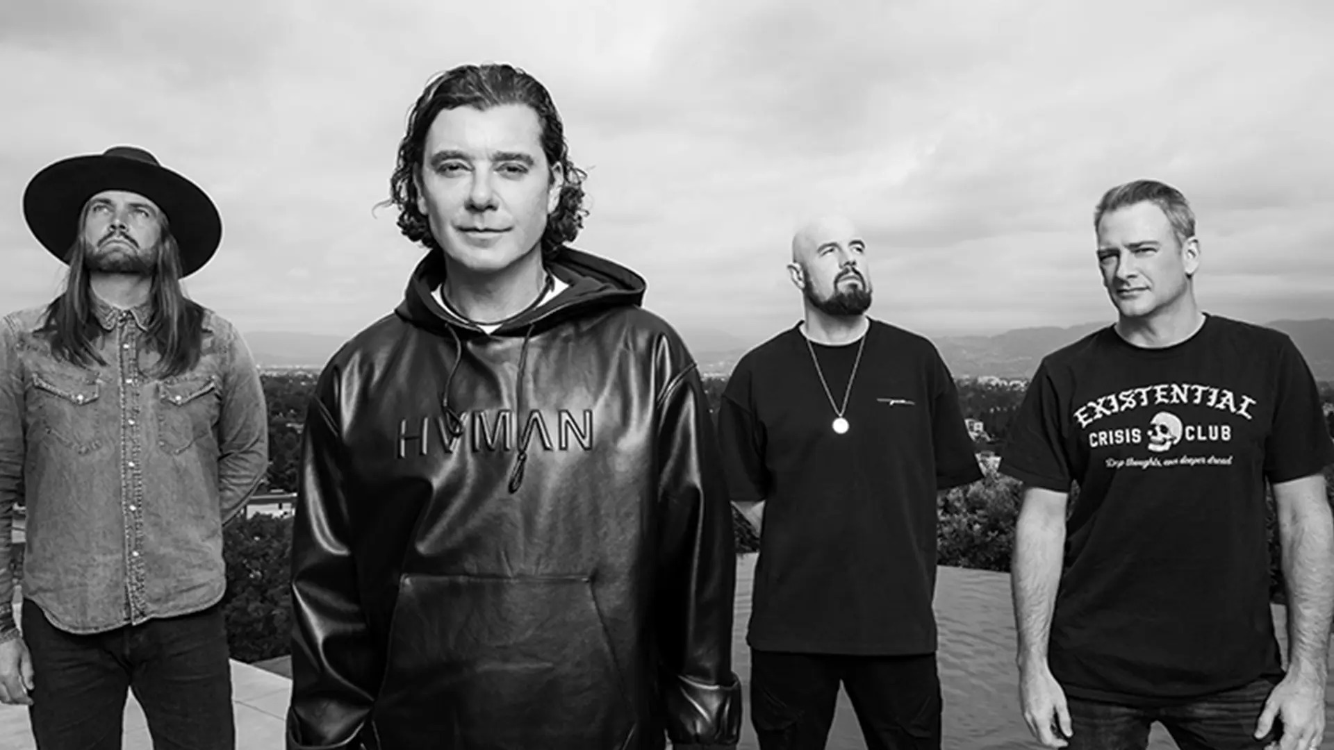Four men stand together against a backdrop of mountains and trees, each dressed in dark clothing with distinctive accessories like hats and necklaces in Williamson County, Tennessee.