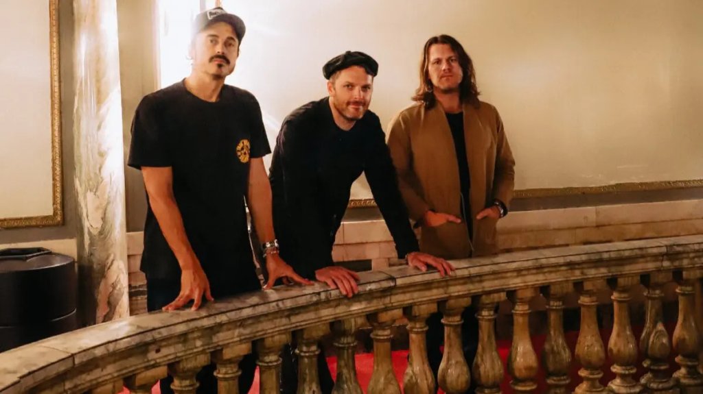 Three men in dark clothing pose together on a grand staircase with ornate railings and a red carpet in Williamson County, Tennessee.