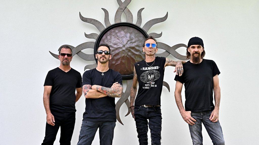 Four men in black t-shirts and sunglasses stand in front of a large sunburst wall sculpture in Williamson County, Tennessee.