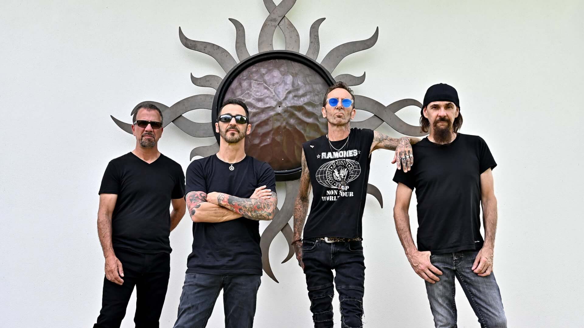 Four men in black t-shirts and sunglasses stand in front of a large sunburst wall sculpture in Williamson County, Tennessee.