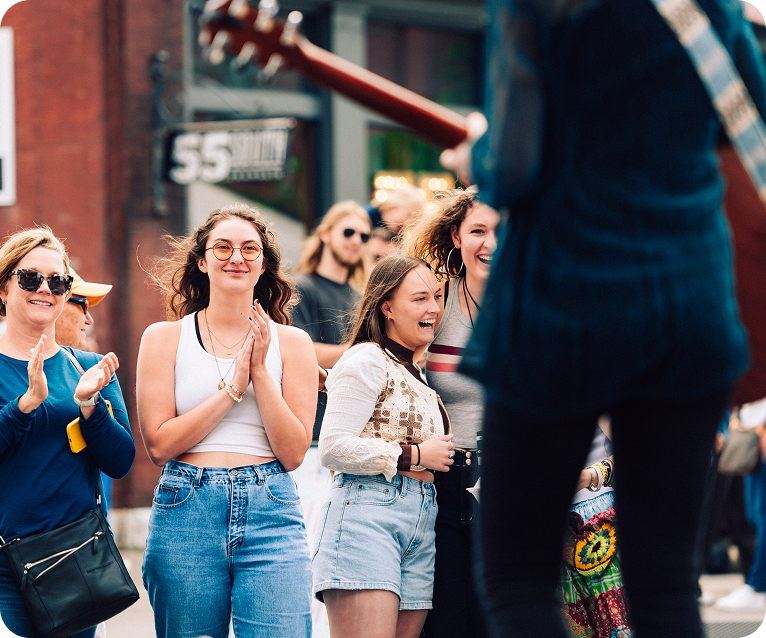 A group of young women, dressed in casual summer attire, are clapping and laughing together on a sunny street in Williamson County, Tennessee.
