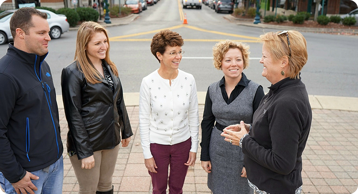 A group of five people, three women and two men, are standing on a sidewalk in a town square, engaged in a lively conversation in Williamson County, Tennessee.