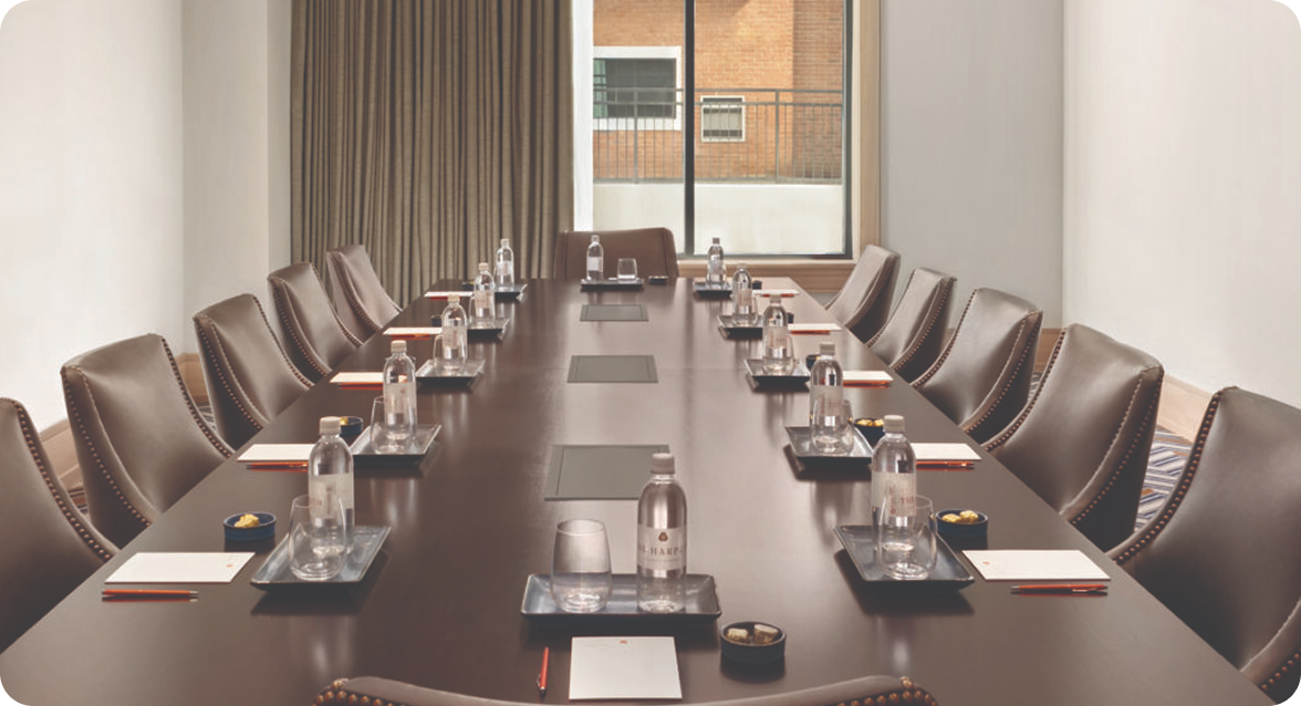 A long, polished wooden conference table is set with water bottles, glasses, and notepads for a meeting, surrounded by comfortable leather chairs in Williamson County, Tennessee.