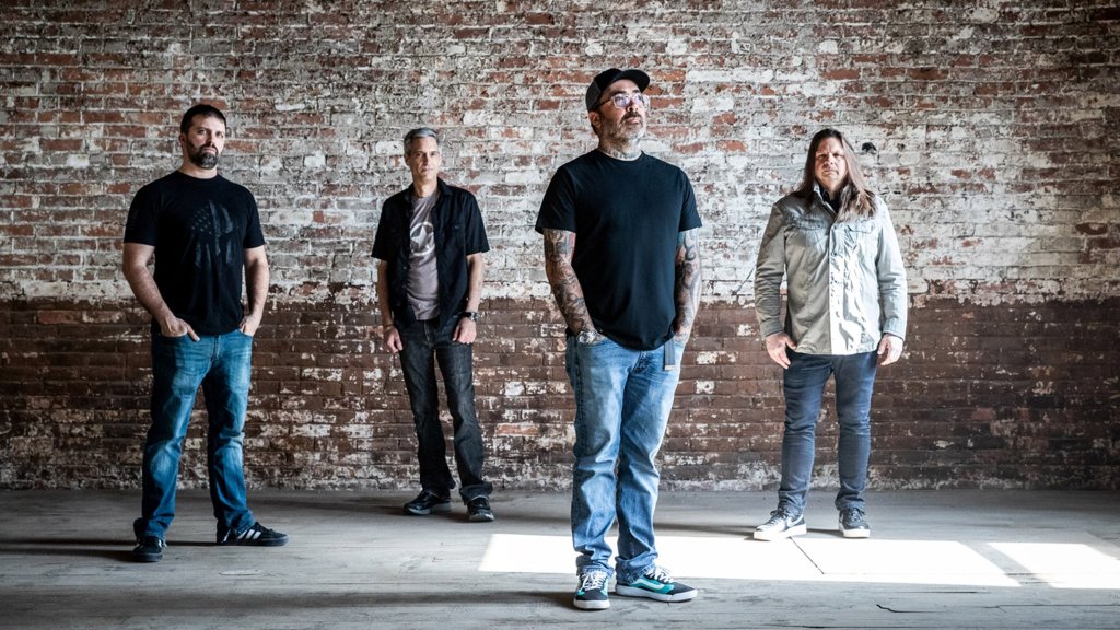 Four men stand in a row against a weathered brick wall, each dressed in casual attire with a mix of jeans, t-shirts, and jackets, exuding a relaxed yet intense presence in Williamson County, Tennessee.