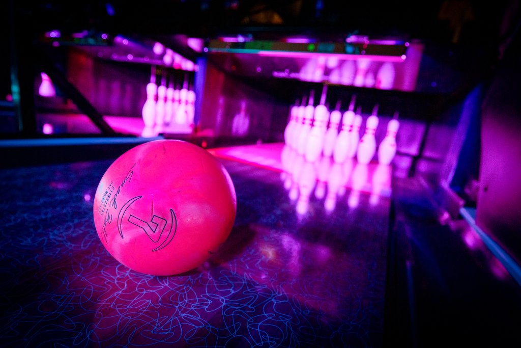 A vibrant pink bowling ball rests on a shimmering, darkly patterned lane, ready to roll towards the glowing purple pins in the distance in Williamson County, Tennessee.