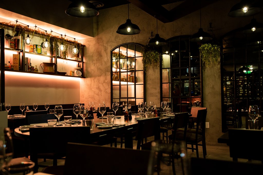 A dimly lit, elegant restaurant with wooden tables set for dining, surrounded by dark leather chairs and illuminated by hanging pendant lights in Williamson County, Tennessee.