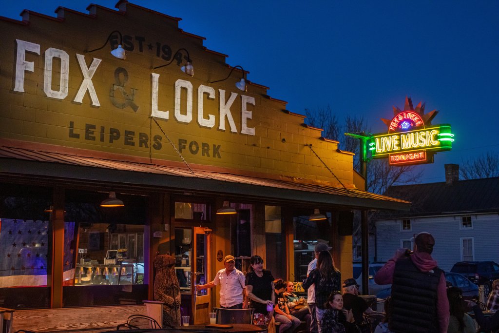 A lively evening scene at Fox & Locke Leipers Fork, with patrons enjoying live music under a neon sign in Williamson County, Tennessee.