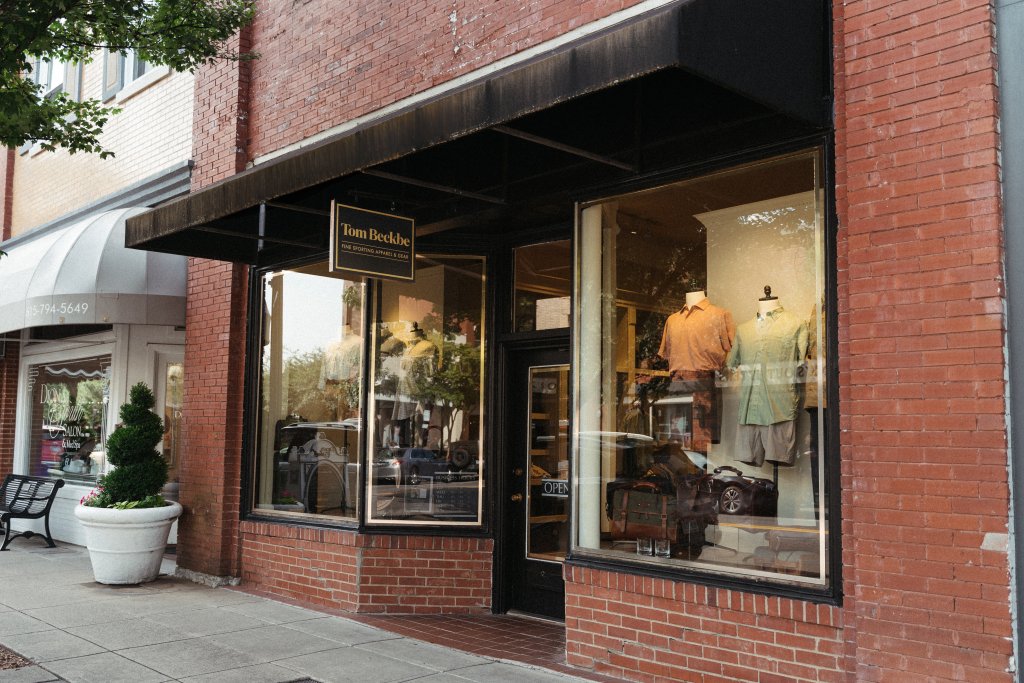 A charming brick storefront with large windows displays a variety of men's clothing and accessories, inviting passersby to explore the stylish offerings inside in Williamson County, Tennessee.