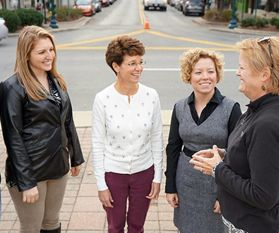 Four women are engaged in a lively conversation on a sunny street corner in Williamson County, Tennessee.