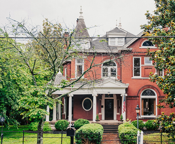 A stately red-brick Victorian house with a wrap-around porch and a distinctive turret stands amidst lush greenery in Williamson County, Tennessee.