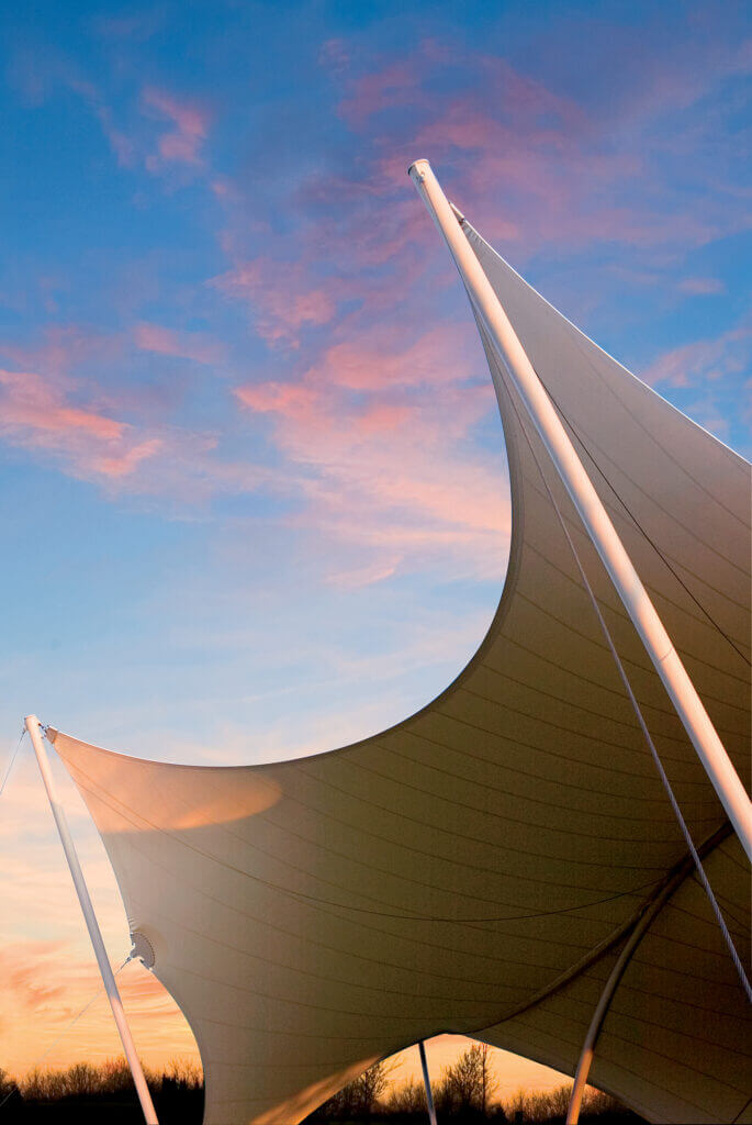 Two large, curved white sails stretch across the sky, creating a dramatic silhouette against a backdrop of vibrant orange and pink hues at sunset in Williamson County, Tennessee.