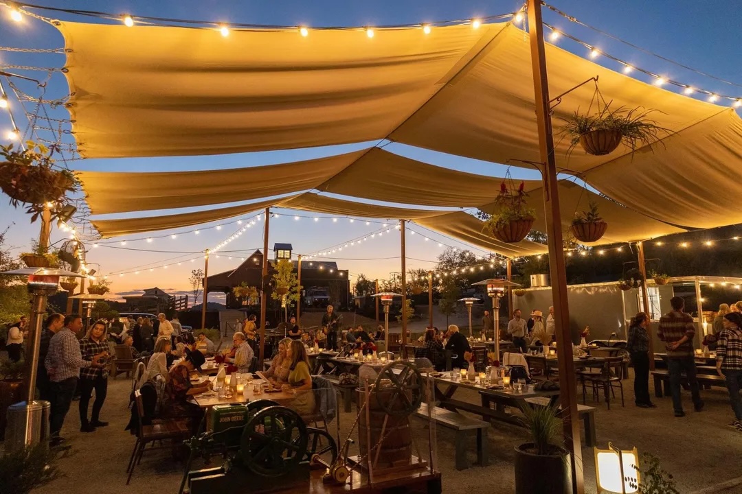 An outdoor dining area with large beige tents illuminated by string lights, filled with people enjoying meals at wooden tables and benches in Williamson County, Tennessee.