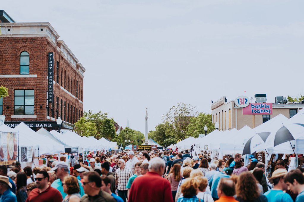 A bustling outdoor market with white tents lines a city street, filled with shoppers and vendors under a clear blue sky in Williamson County, Tennessee.