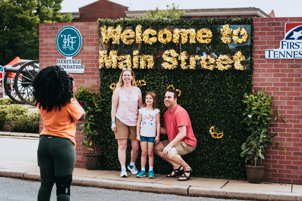 A family of four poses for a photo in front of a floral welcome sign on Main Street in Williamson County, Tennessee.