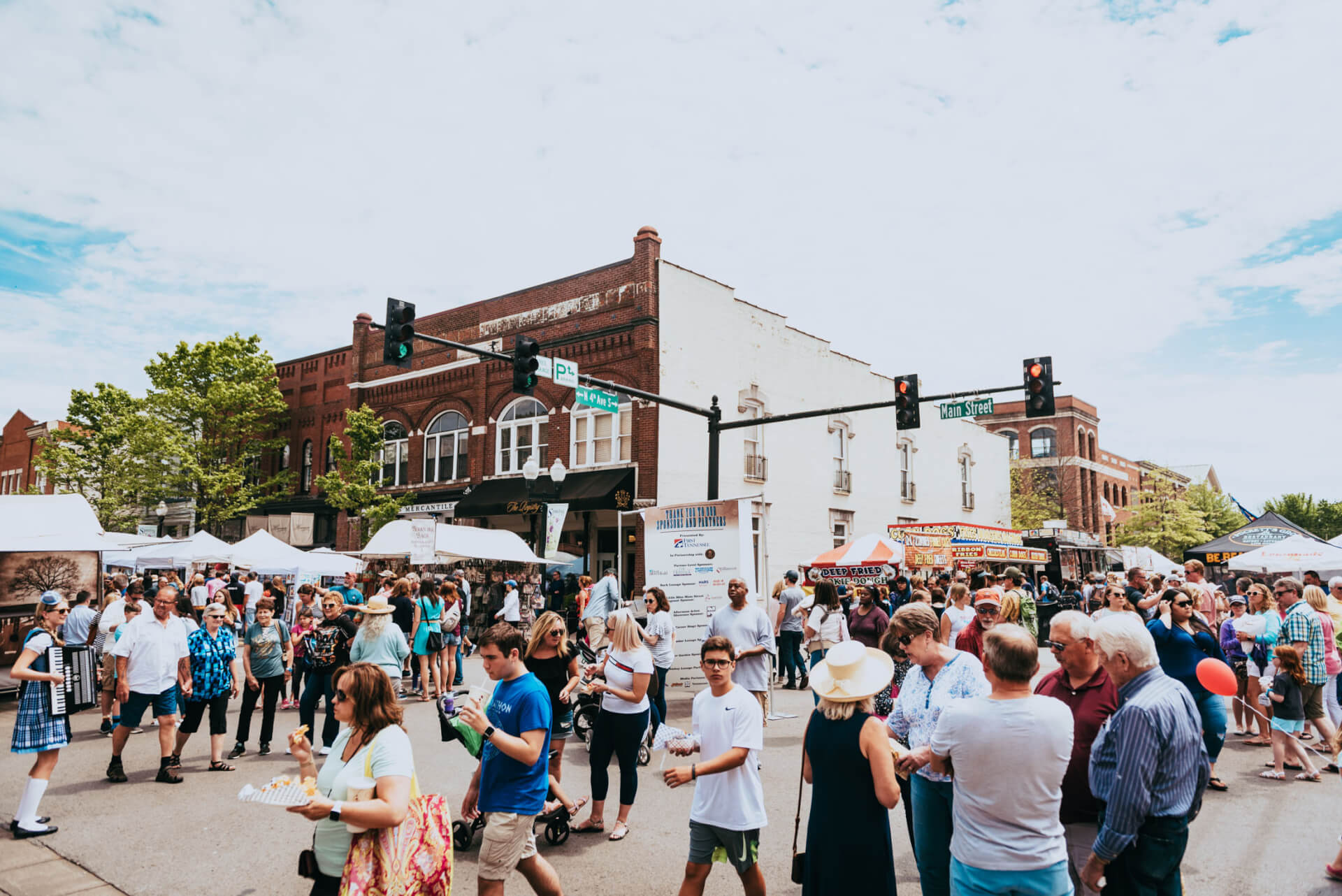 A bustling outdoor market fills a town square with people browsing stalls, enjoying food, and listening to live music under a clear blue sky in Williamson County, Tennessee.