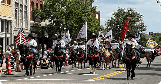 A parade featuring a group of riders on horseback, each carrying flags, marches down a town street lined with spectators in Williamson County, Tennessee.