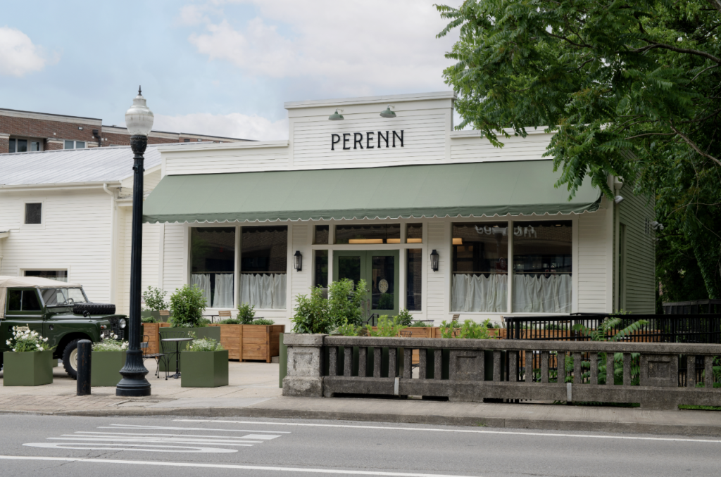A charming white building with a green awning and the sign 'PERENN' above the entrance, featuring a quaint outdoor seating area with green planters and a vintage green truck parked nearby in Williamson County, Tennessee.