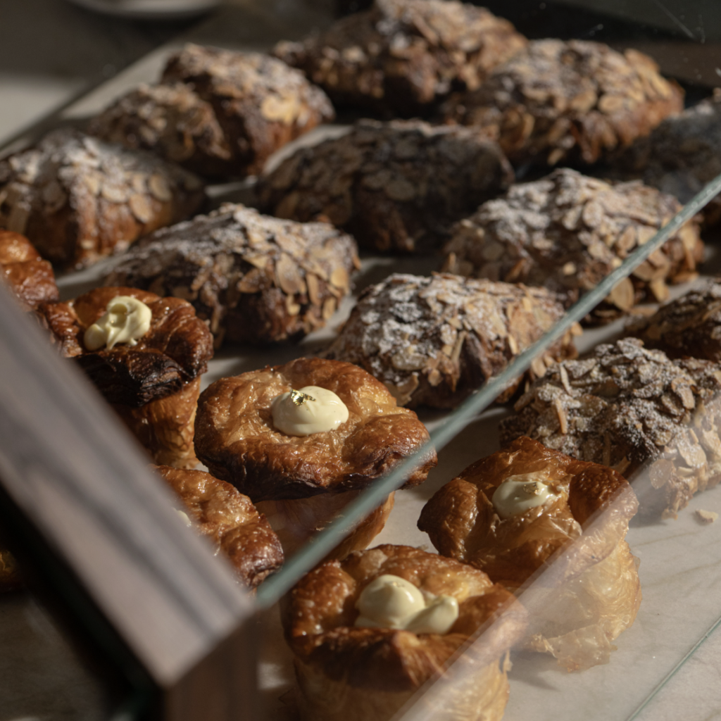A variety of freshly baked pastries, including croissants, almond-topped treats, and creamy-filled pastries, are displayed in a glass case at a bakery in Williamson County, Tennessee.
