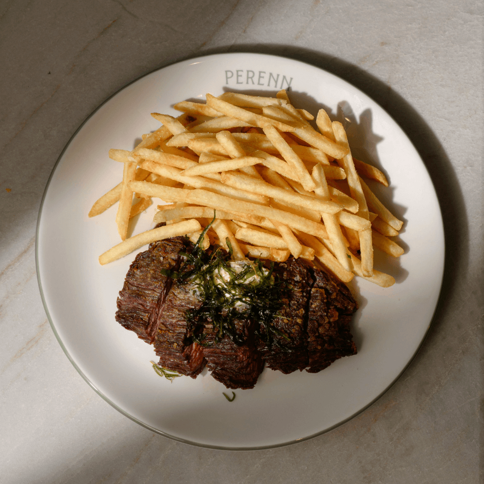 A plate of medium-rare steak slices topped with herbs, accompanied by a generous serving of golden-brown french fries in Williamson County, Tennessee.